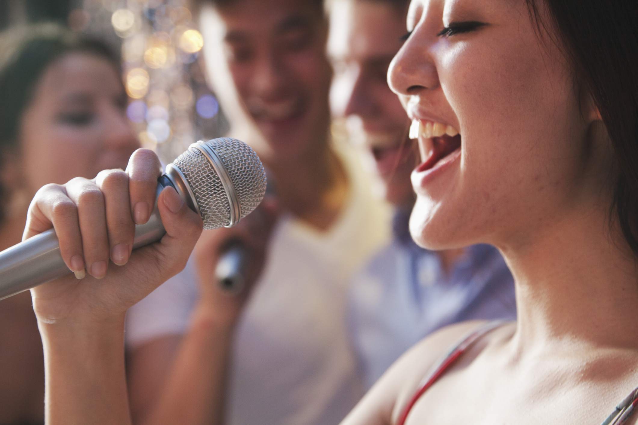 En närbild av en kvinna som sjunger in i en mikrofon med vänner i bakgrunden