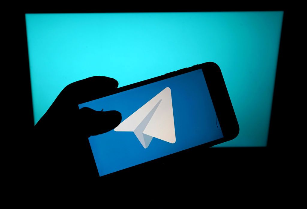Telegram-logotypen på en smartphone silhuett mot en blå bakgrund.