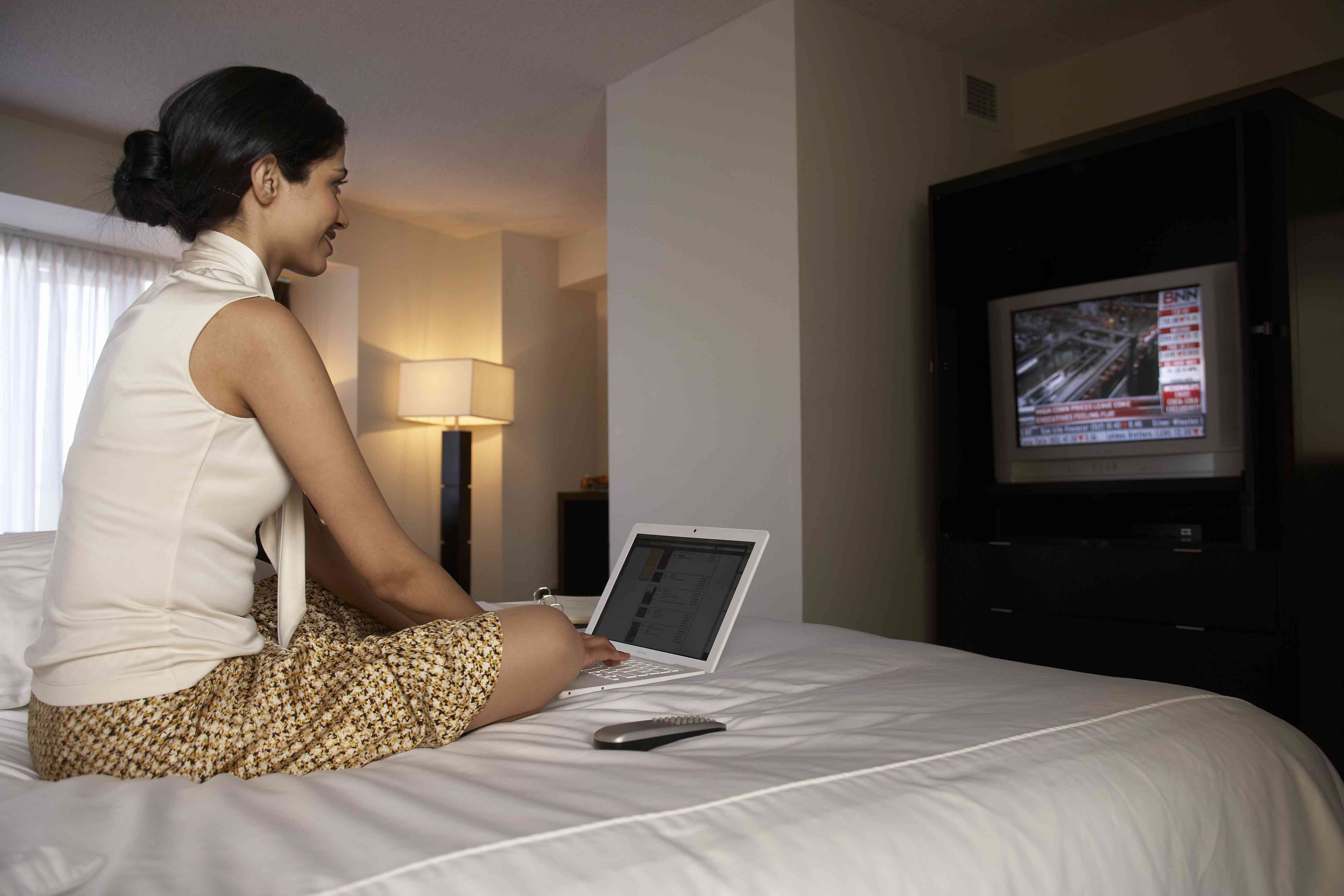 Kvinna på hotellsäng med bärbara datorn som håller ögonen på finansiella nyheter