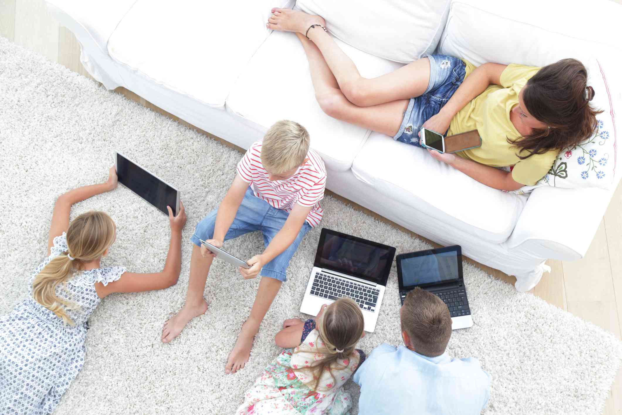 En familj på fem som alla använder tekniska enheter i vardagsrummet. 