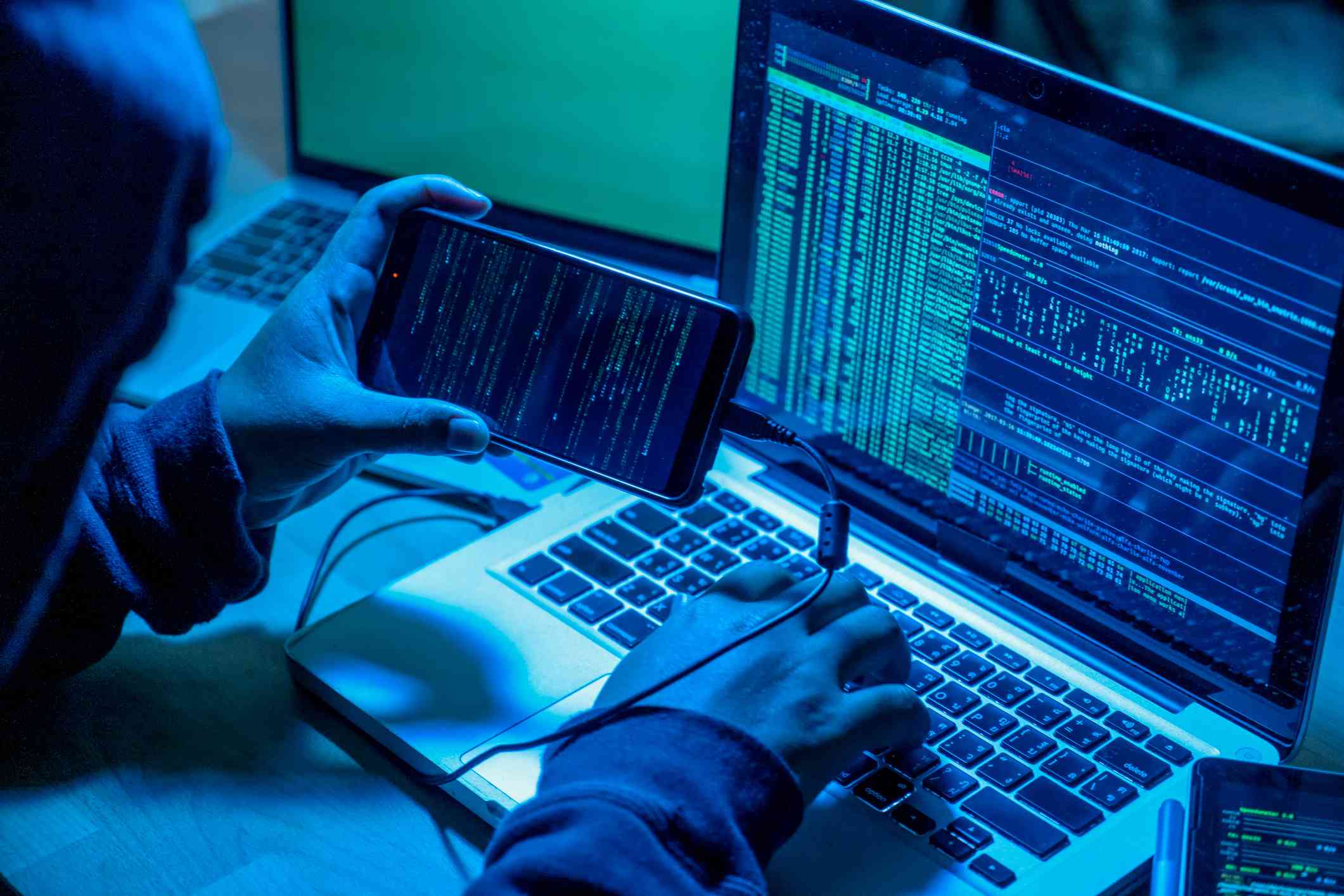 Hacker med smartphone och datorer i mörkt rum
