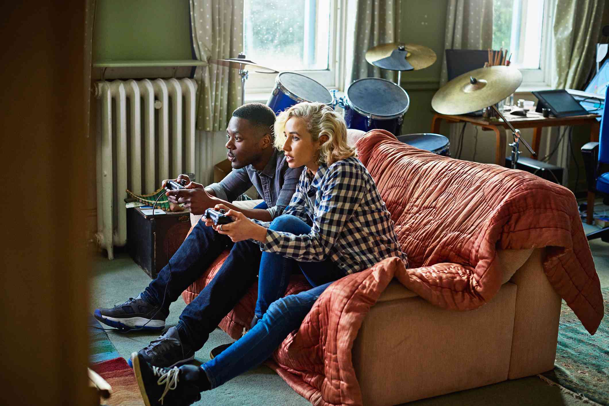 Två unga vuxna som spelar konsolvideospel som sitter på en soffa i en liten lägenhet.