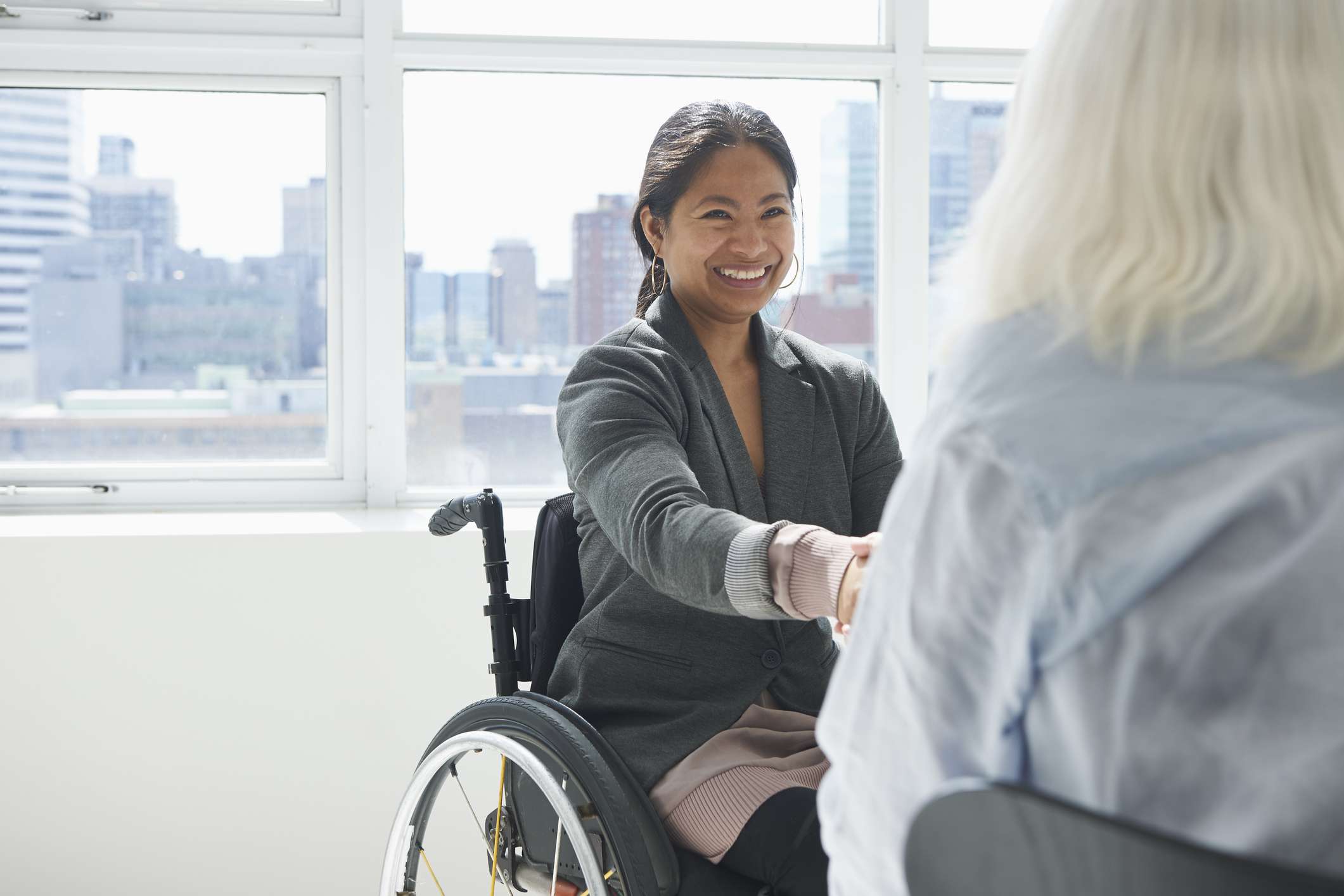 Affärskvinna i en rullstol som skakar hand med en annan person