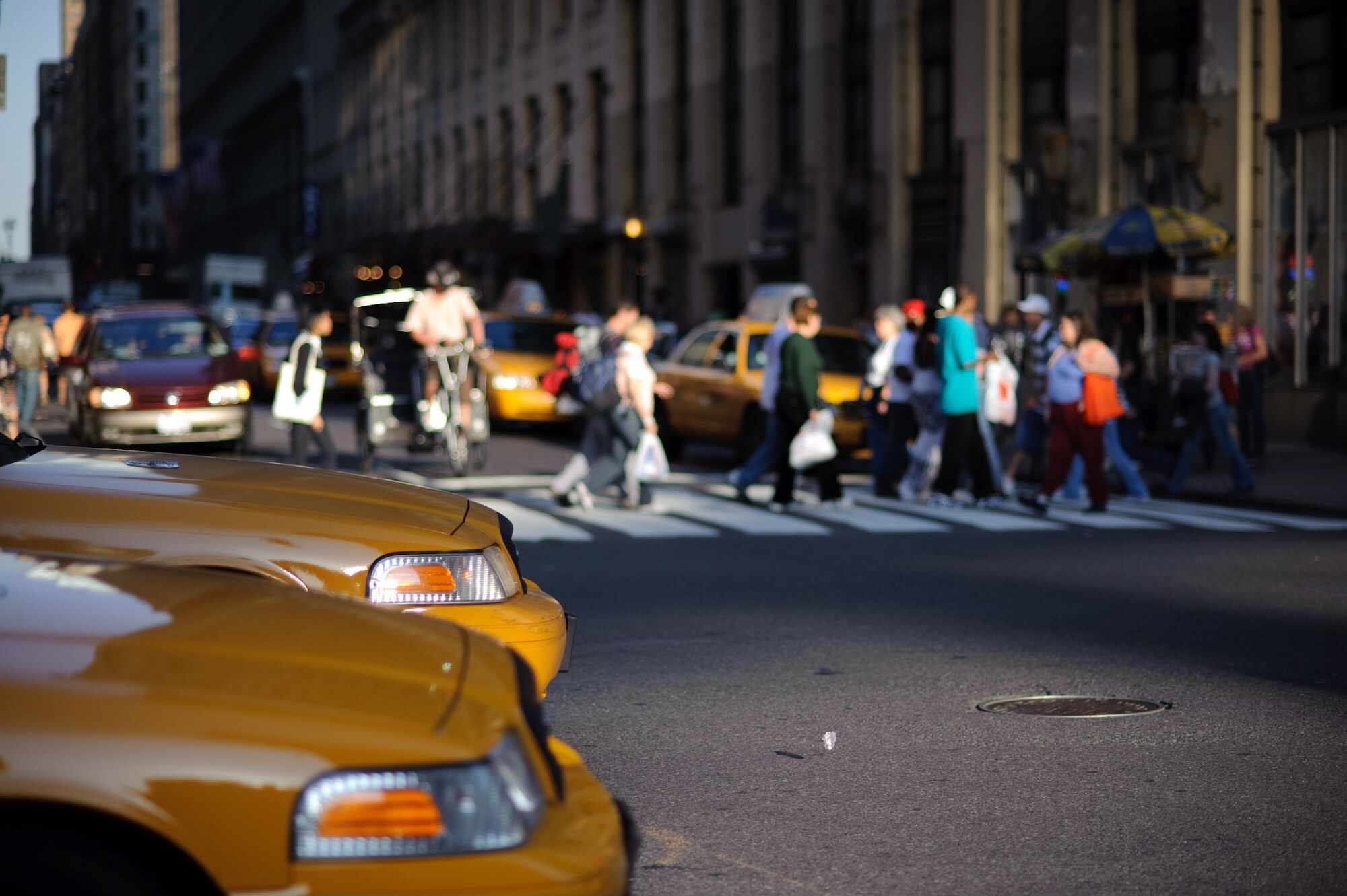 Par taxibilar som väntar vid en korsning medan folk korsar gatan i bakgrunden