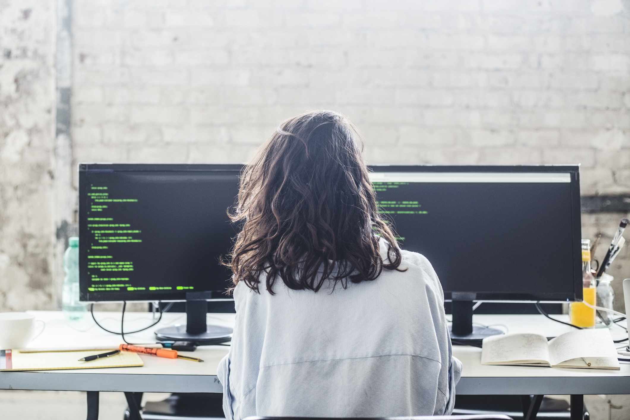 Bakre sikt av kvinnlig datahackare som kodar på skrivbordet i idérikt kontor