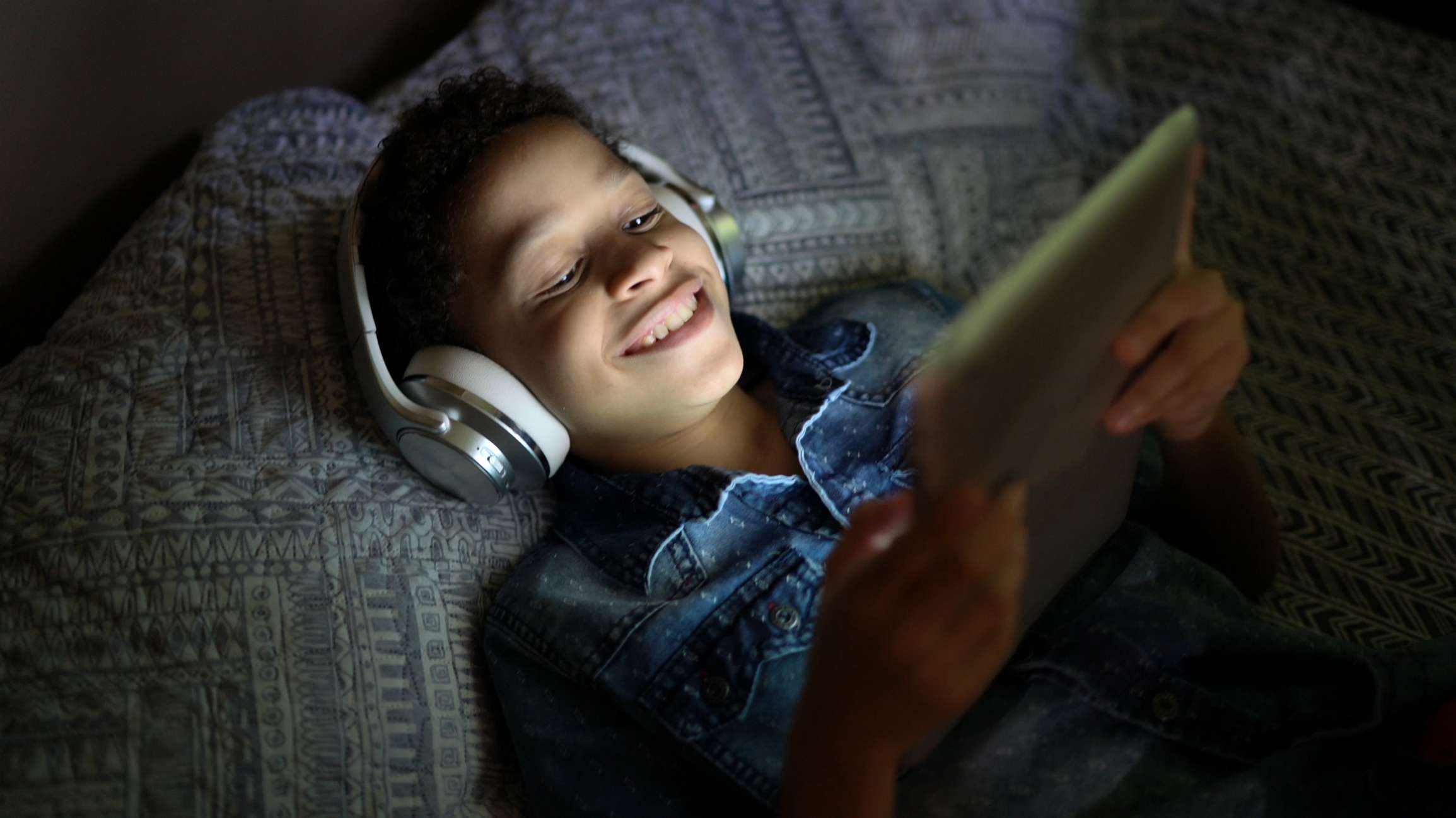En tonåring som lägger i säng som håller ögonen på en film på en minnestavla. 