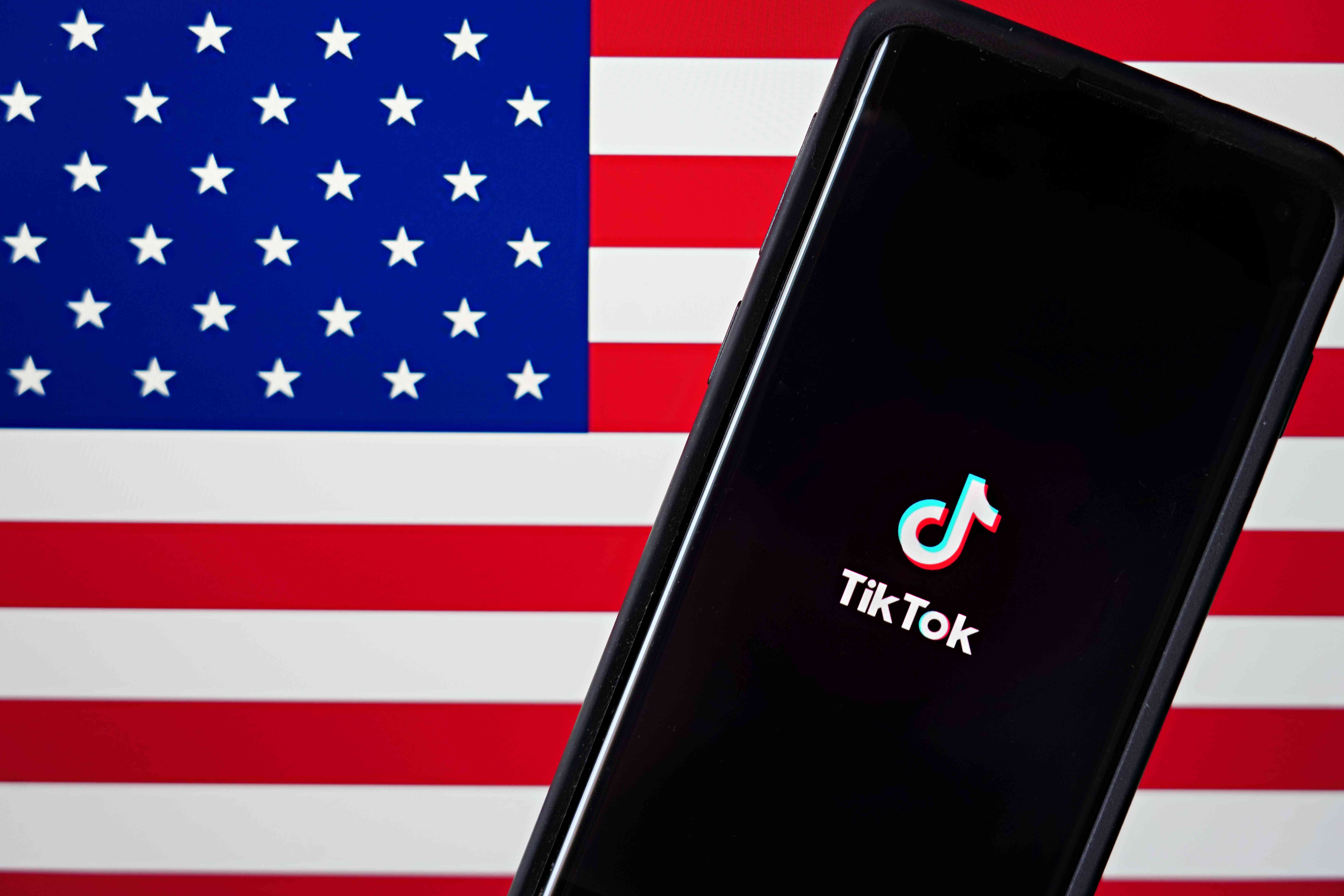 En mobiltelefon med TikTok-appen visas bredvid den amerikanska flaggan