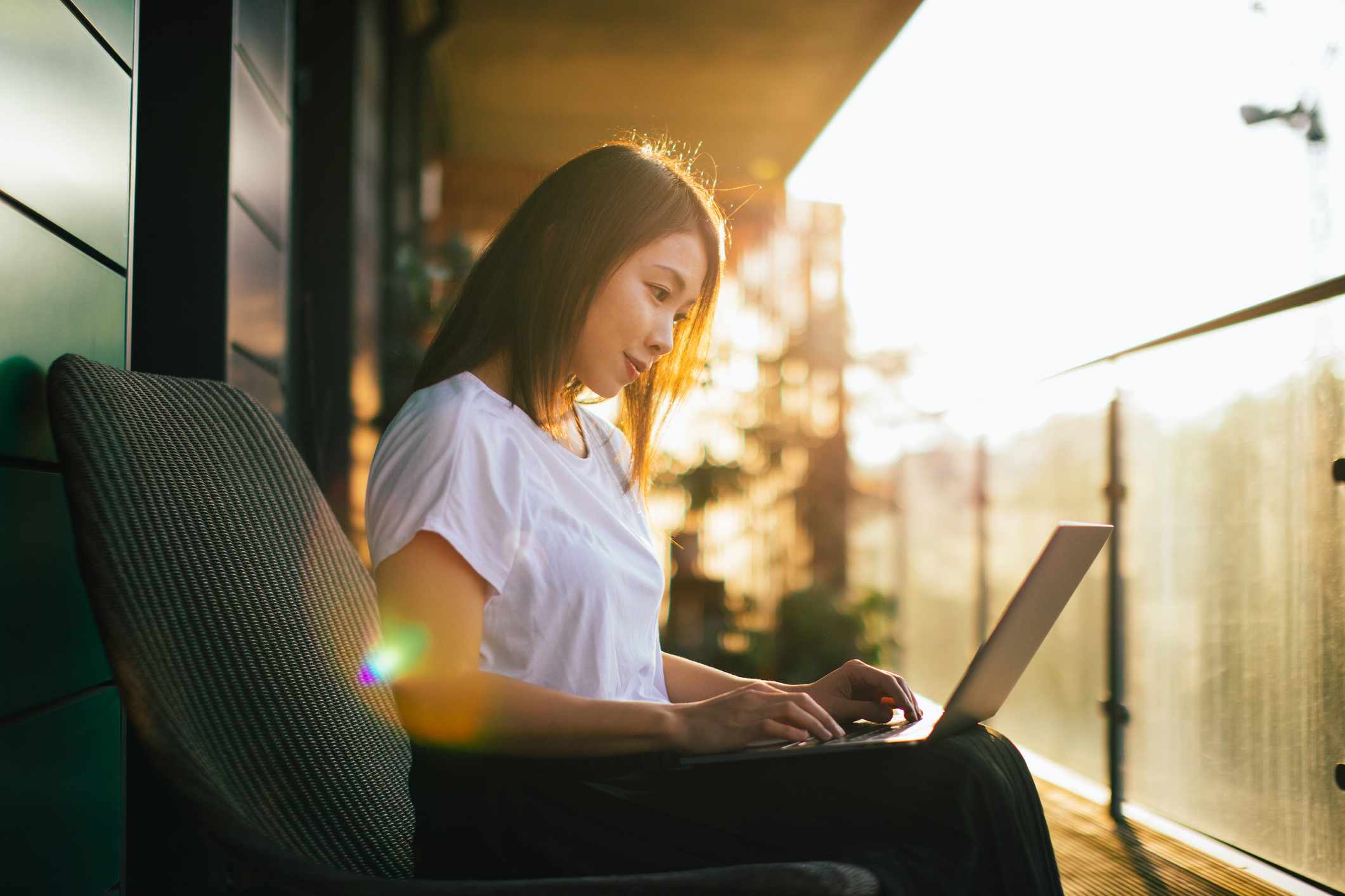 Kvinna som arbetar med datoren på hennes knä som sitter på balkongen vid solnedgångtid