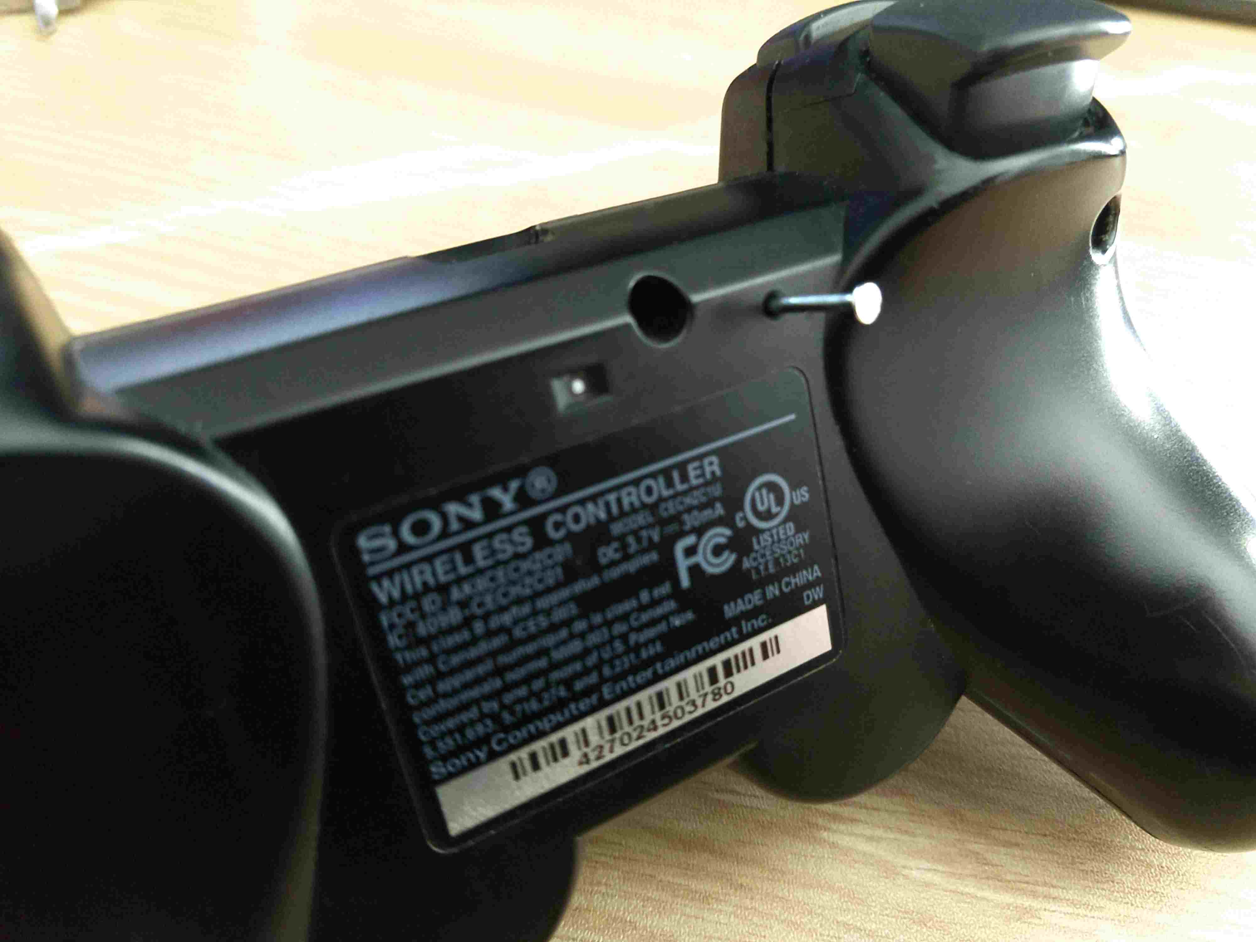 Ett verktyg infogat i återställningsknappens åtkomsthål på en PS3-kontroller