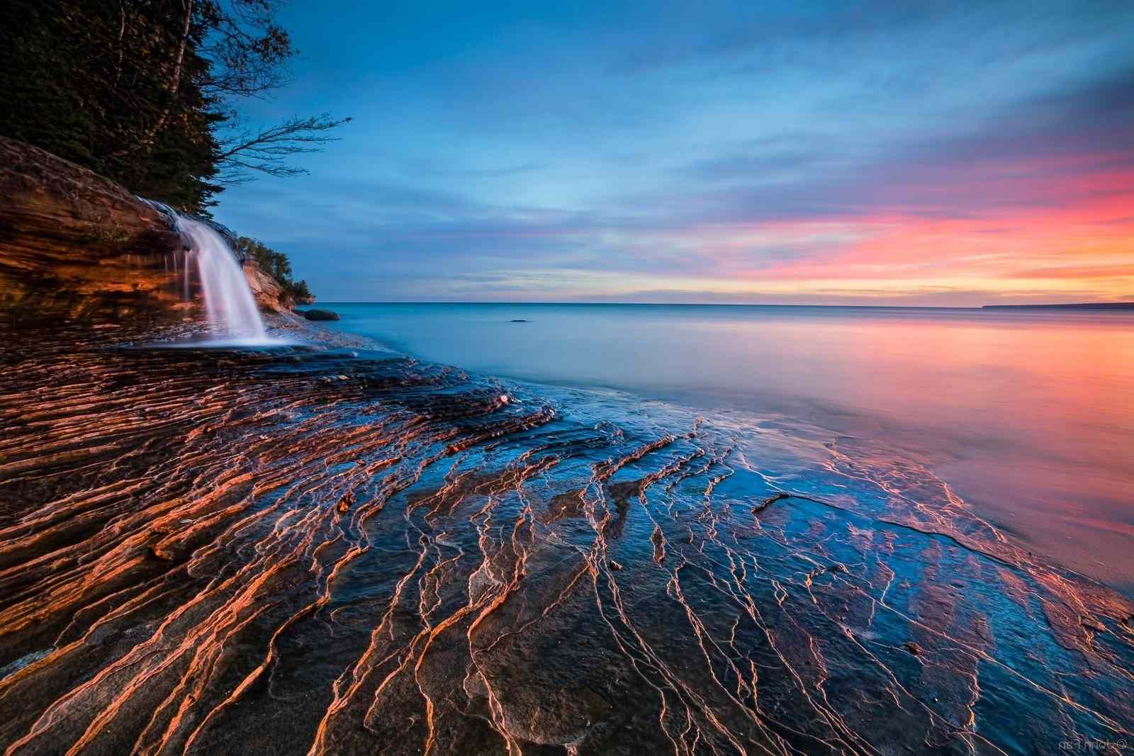 Ett litet vattenfall på en strand vid solnedgången i denna fria havstapet