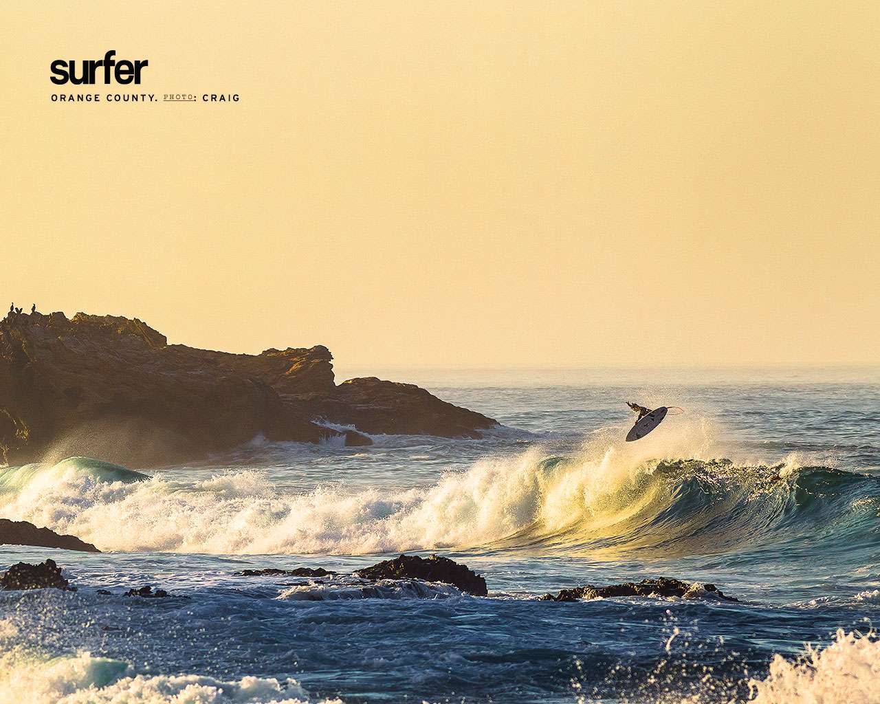 Gratis havstapet med en surfare mitt i vändningen ovanför en våg nära klippor och klippor