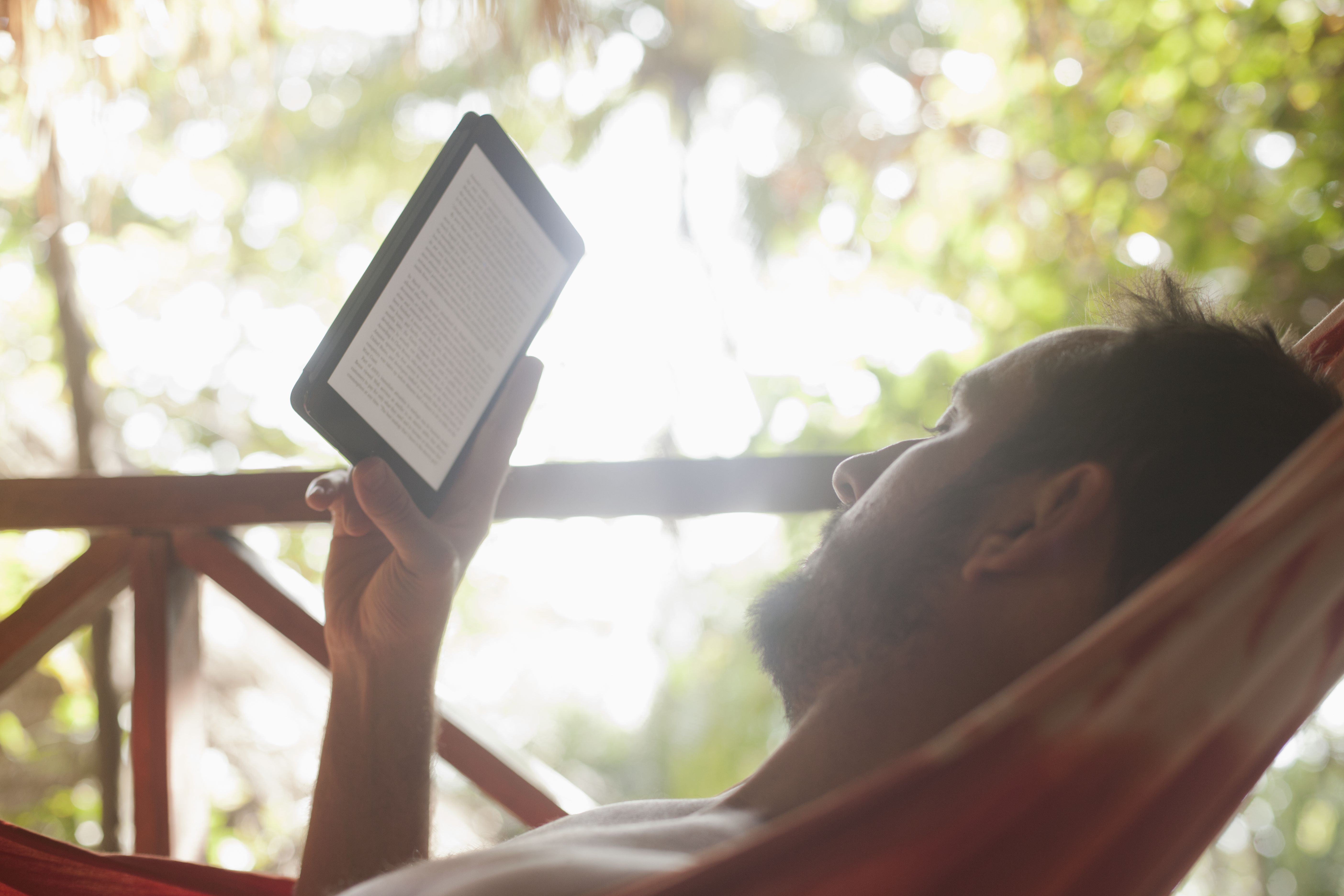 Man som kopplar av i en hängmatta som läser från en digital bok