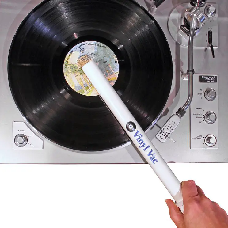 En hand som håller en Vinyl Vac för att rengöra en skiva som ligger ovanpå en skivspelare