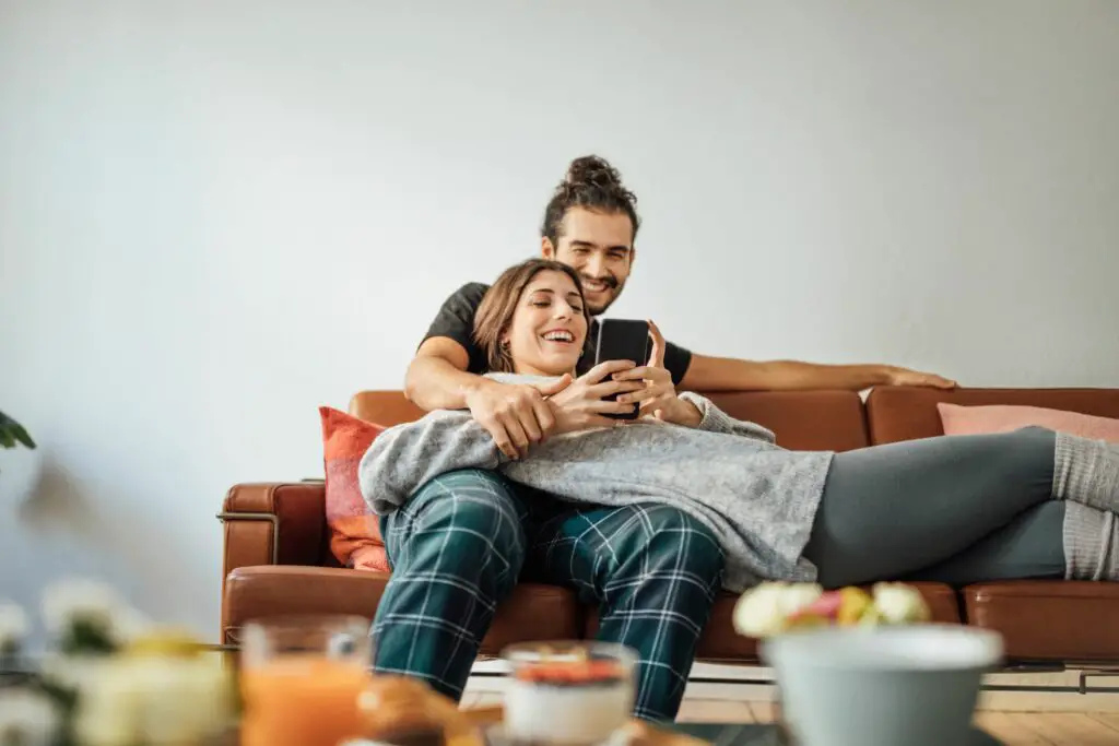 young couple with smart phone relaxing on sofa 974230862 5c4b4d5ec9e77c00013801fc
