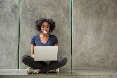 Afroamerikansk högskolestudent som använder bärbar dator och blåser bubbelgummibubbla