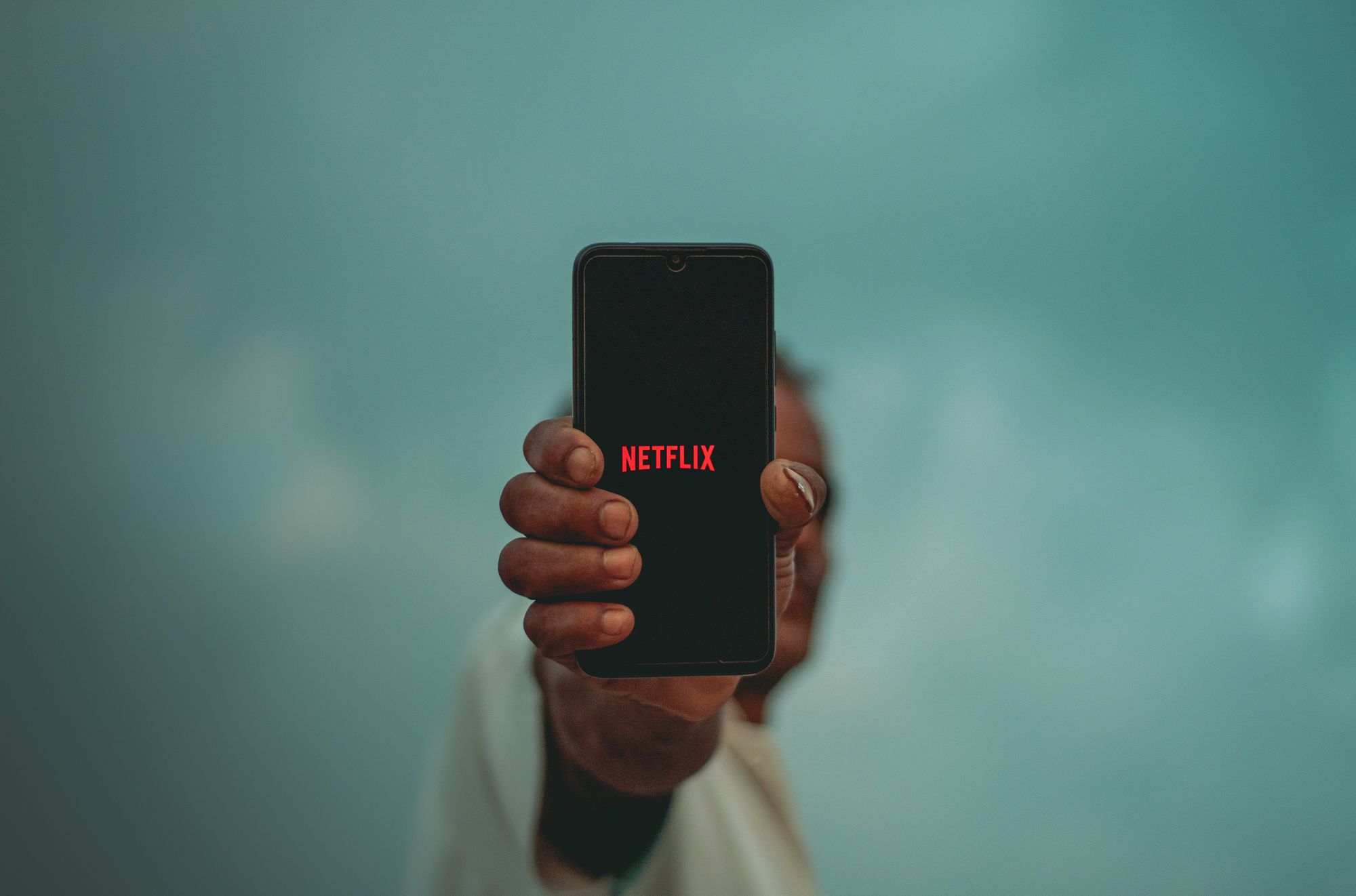 En person som håller en svart iPhone på armlängds avstånd med Netflix-logotypen på skärmen. 