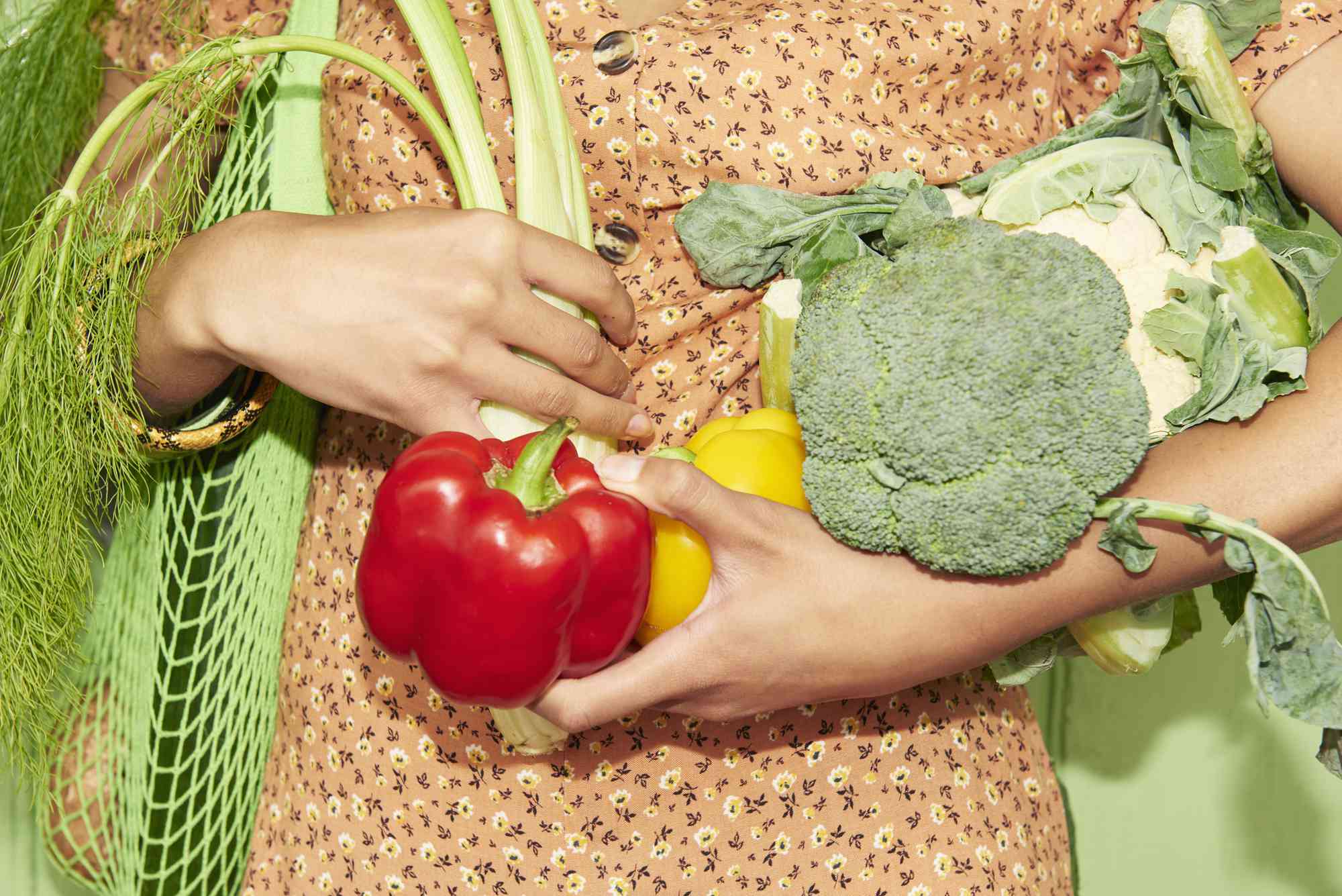 Närbild av någon som håller en armfull färska grönsaker.