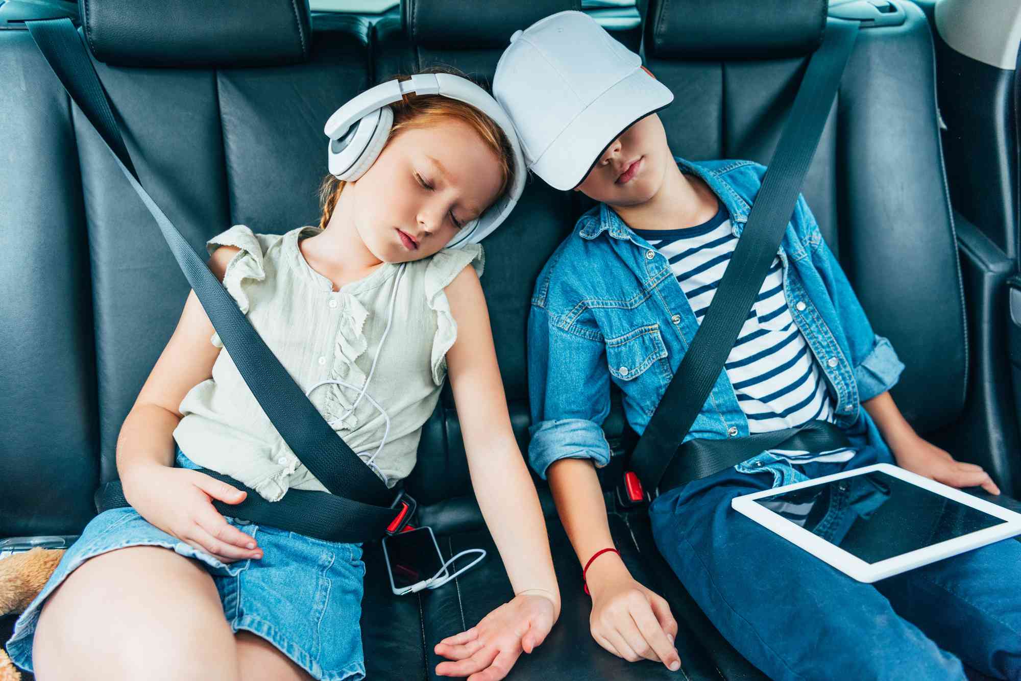 Två barn sover i bilen med elektroniska apparater som kan användas för skolarbete. 