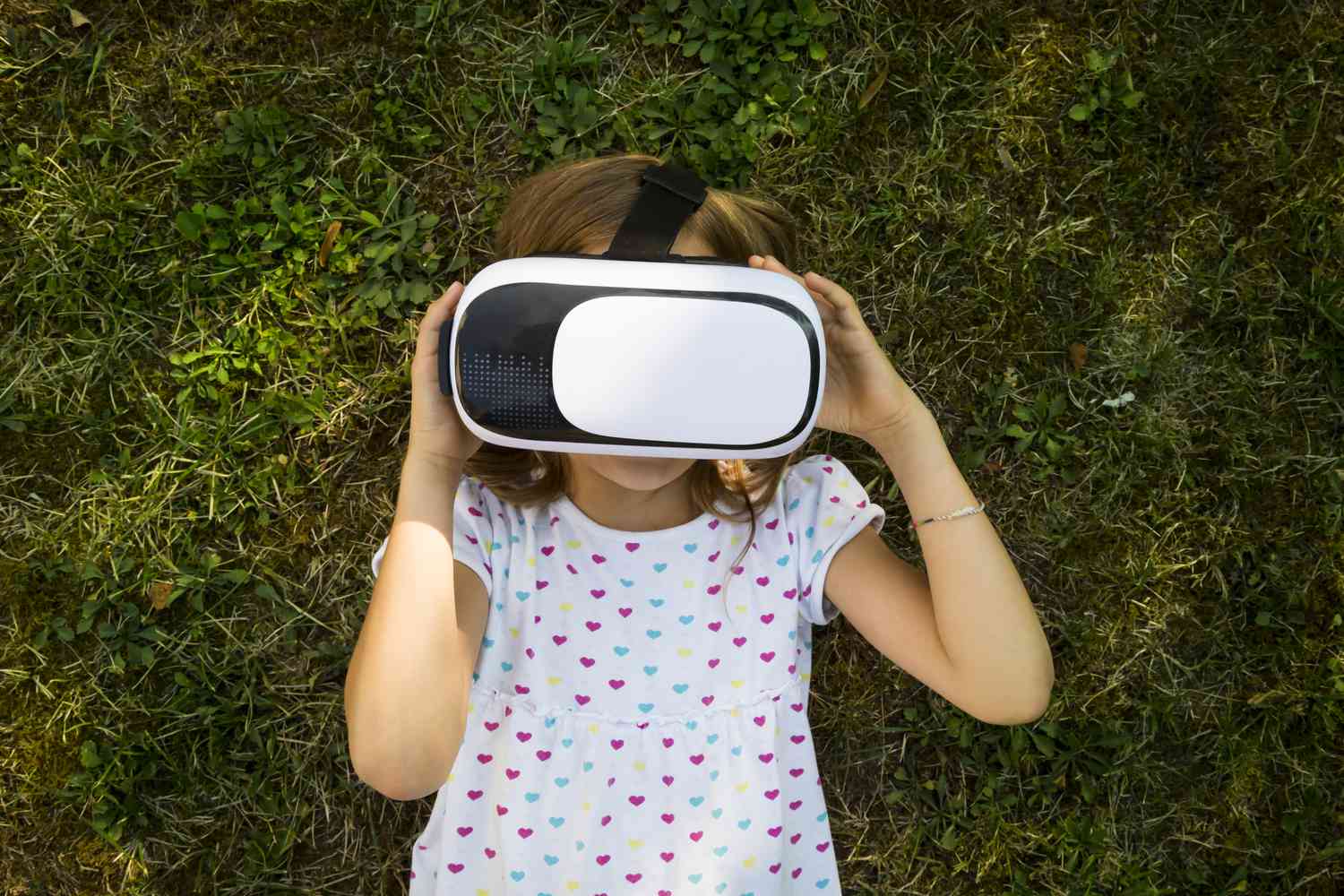 Ett barn med VR-glasögon liggande på marken i en trädgård. 