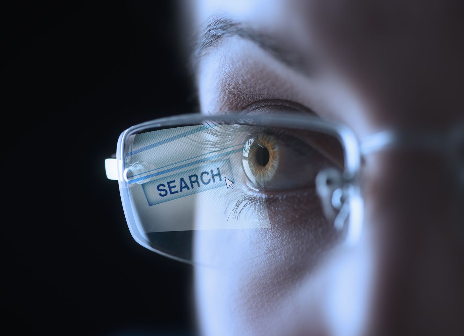 Coseup av ett mänskligt öga, bär glasögon med en sökknapp som reflekterar på linsen.